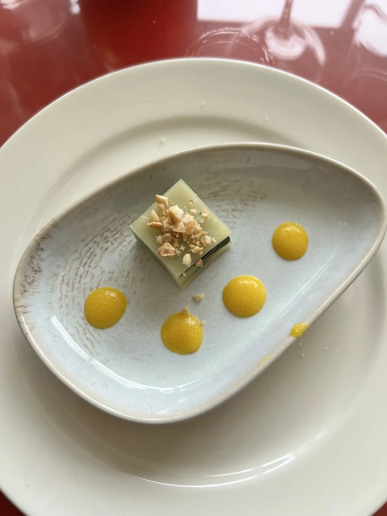 A small plated dessert with dots of yellow sauce on a scalloped dish