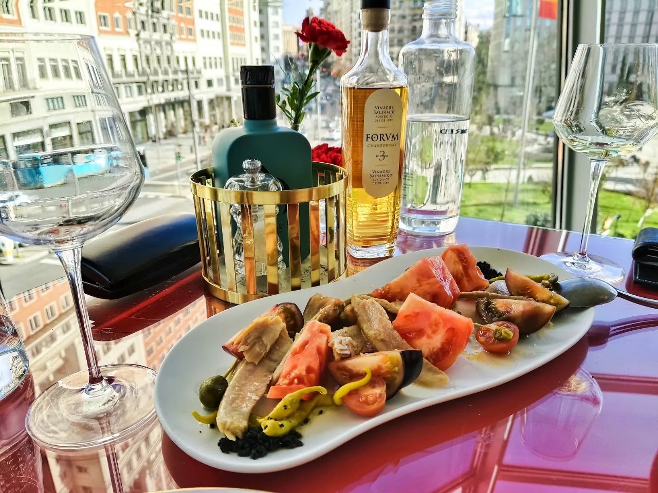 A platter of grilled seafood and charred vegetables beside wine glasses and a bottle