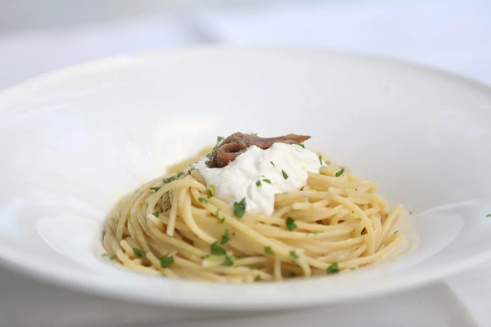 A plate of spaghetti topped with a dollop of burrata and anchovies