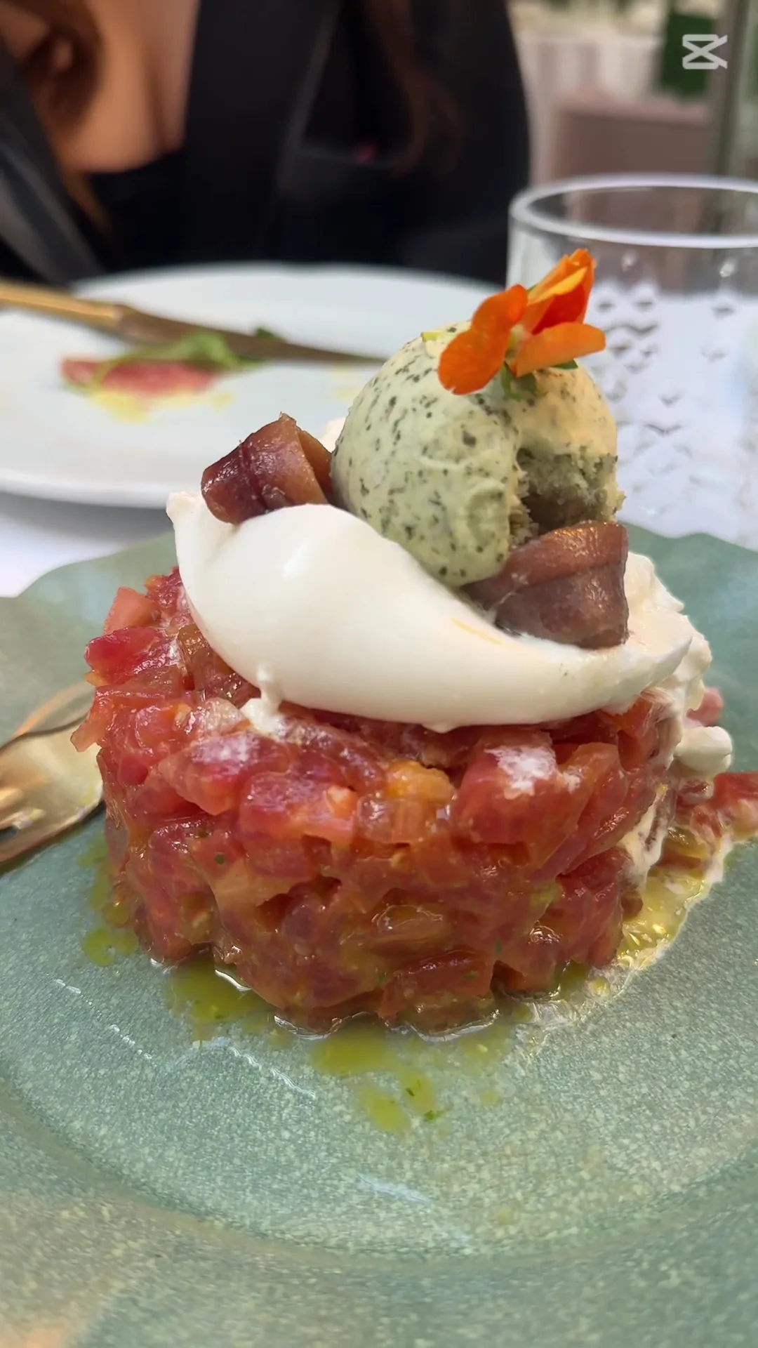 A tuna tartare quenelle topped with a herb-flecked cream and an edible flower