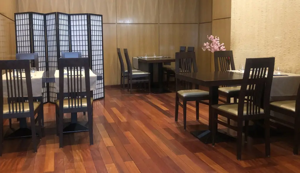 Japanese-style dining room with dark wood tables and slatted chairs, a black shoji folding screen, reddish wood floor and a spray of pink cherry blossom