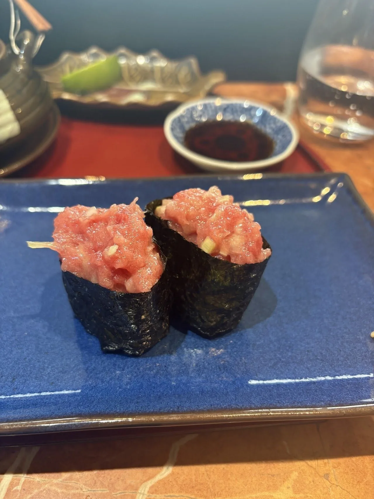 Two gunkan sushi topped with minced fish on a blue plate