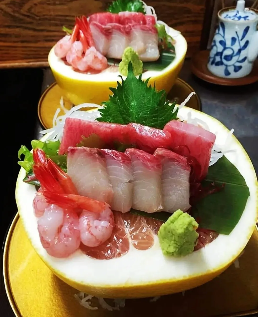 Sashimi slices with a green leaf and wasabi served in a hollowed citrus shell