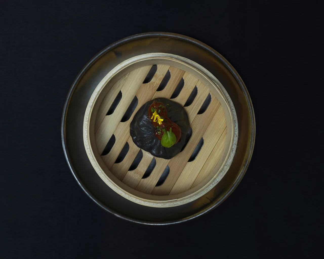 A bamboo steamer seen from above holding a dark dumpling
