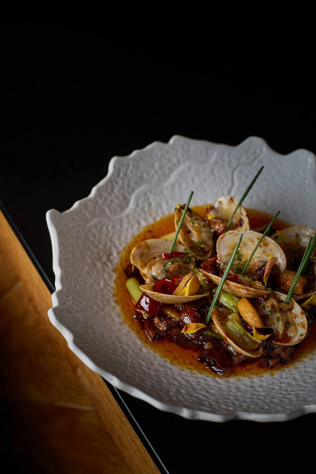 A white ruffled bowl of clams in a light sauce with herbs