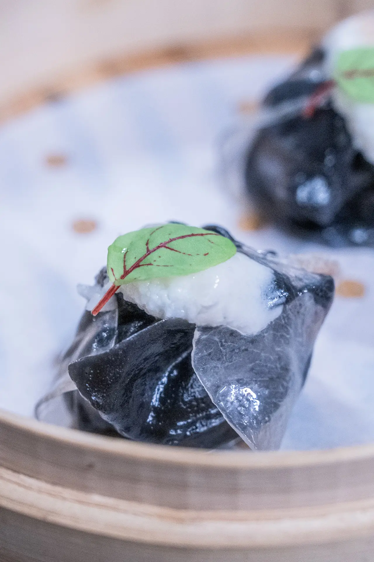 Black dumpling with white filling and a leaf garnish in a bamboo steamer