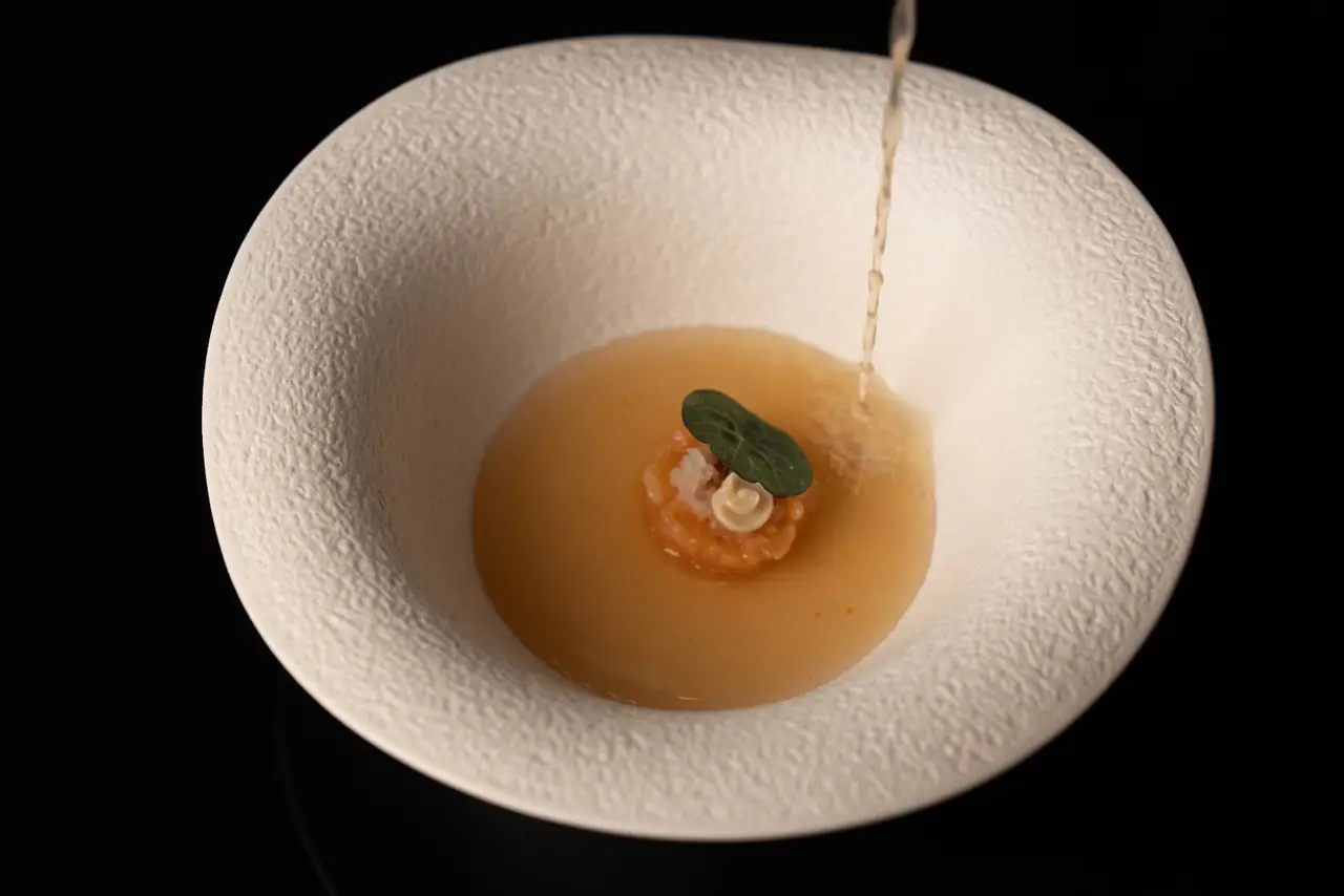 Broth being poured into a white textured bowl over a small tartare bite with leaf garnish