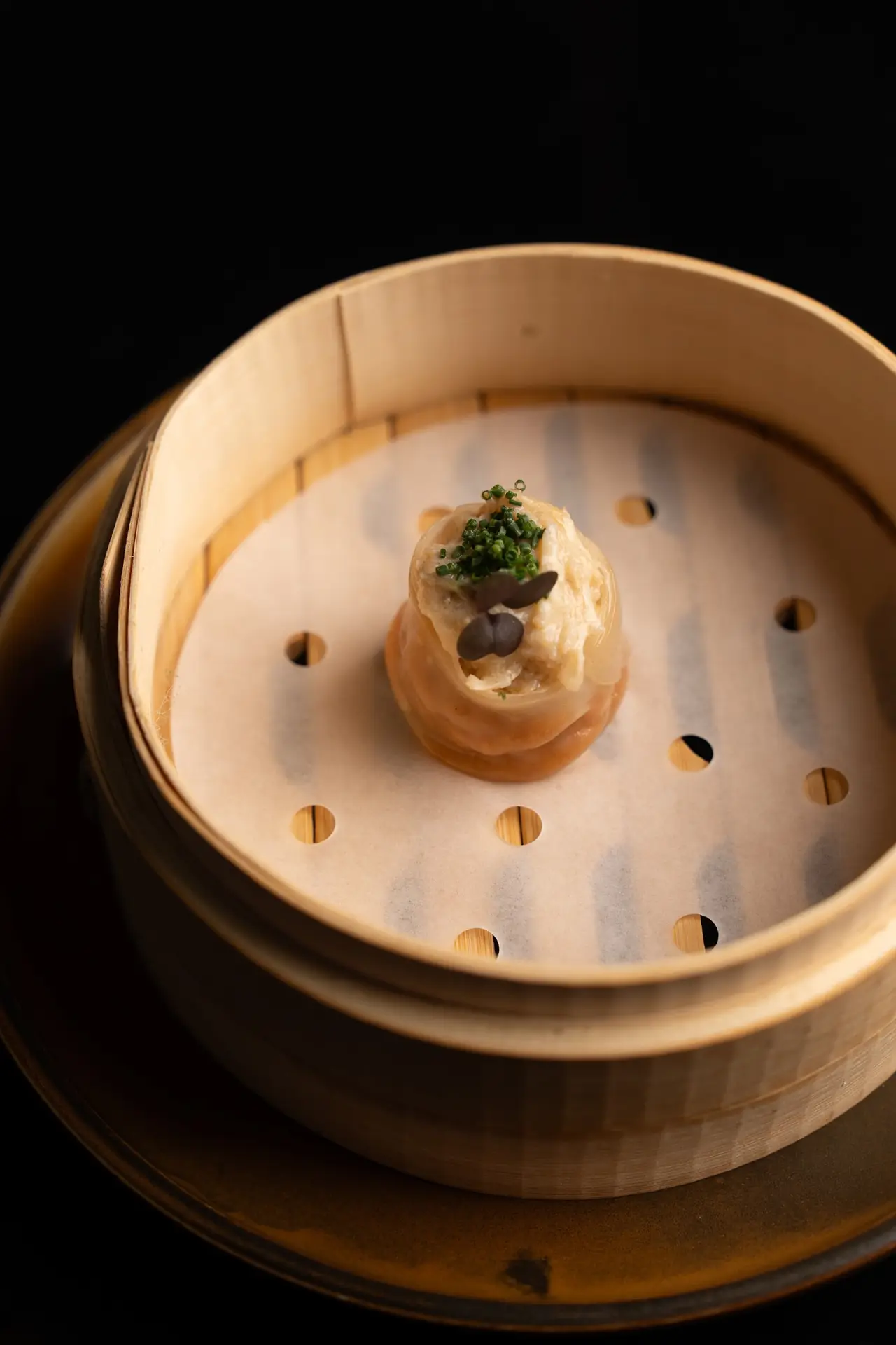 Open-top dumpling with chive garnish in a bamboo steamer