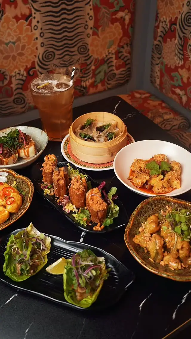 Table spread of Asian small plates including steamed dumplings, lettuce wraps, and a fried snack platter with an iced tea