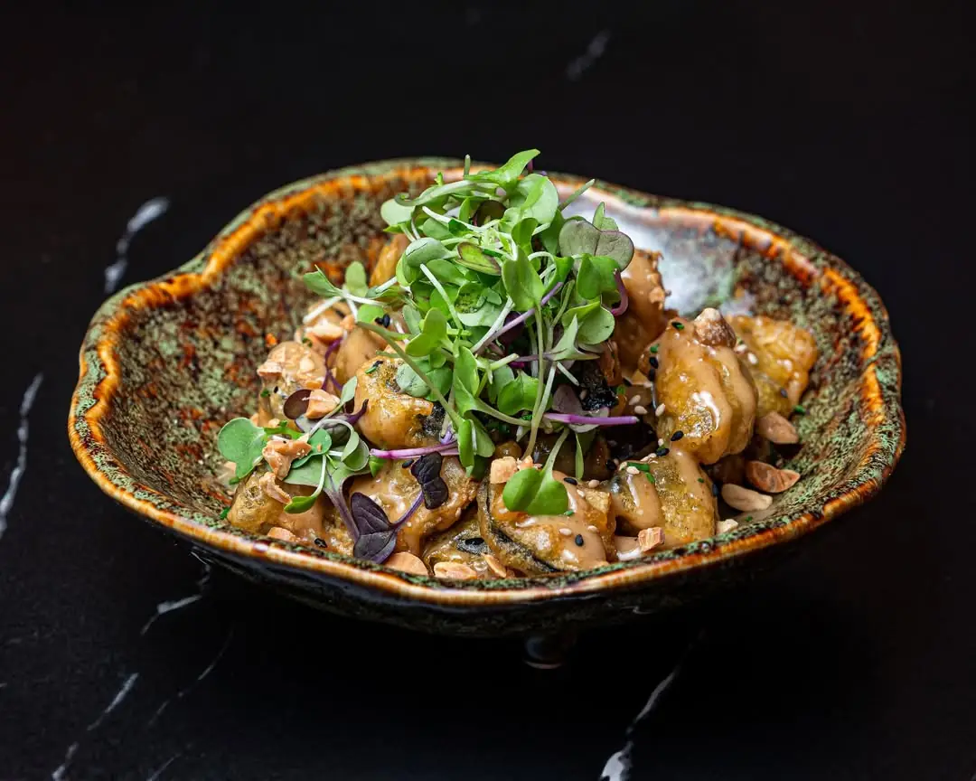 Bowl of glazed chicken bites topped with microgreens, almonds, and sesame seeds