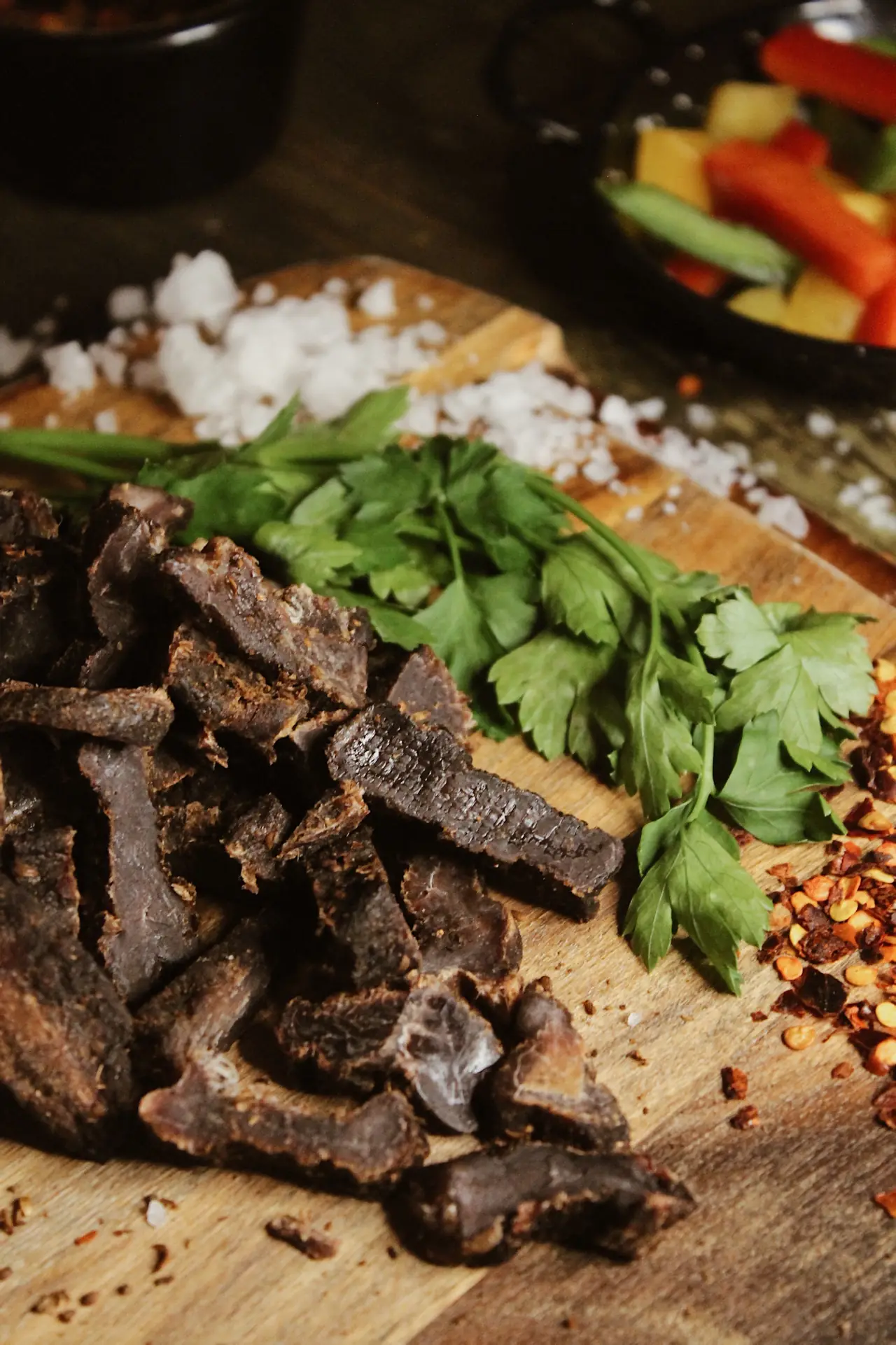 Sliced biltong piled on a wooden board with fresh parsley, coarse salt, and chili flakes, at Spice BCN