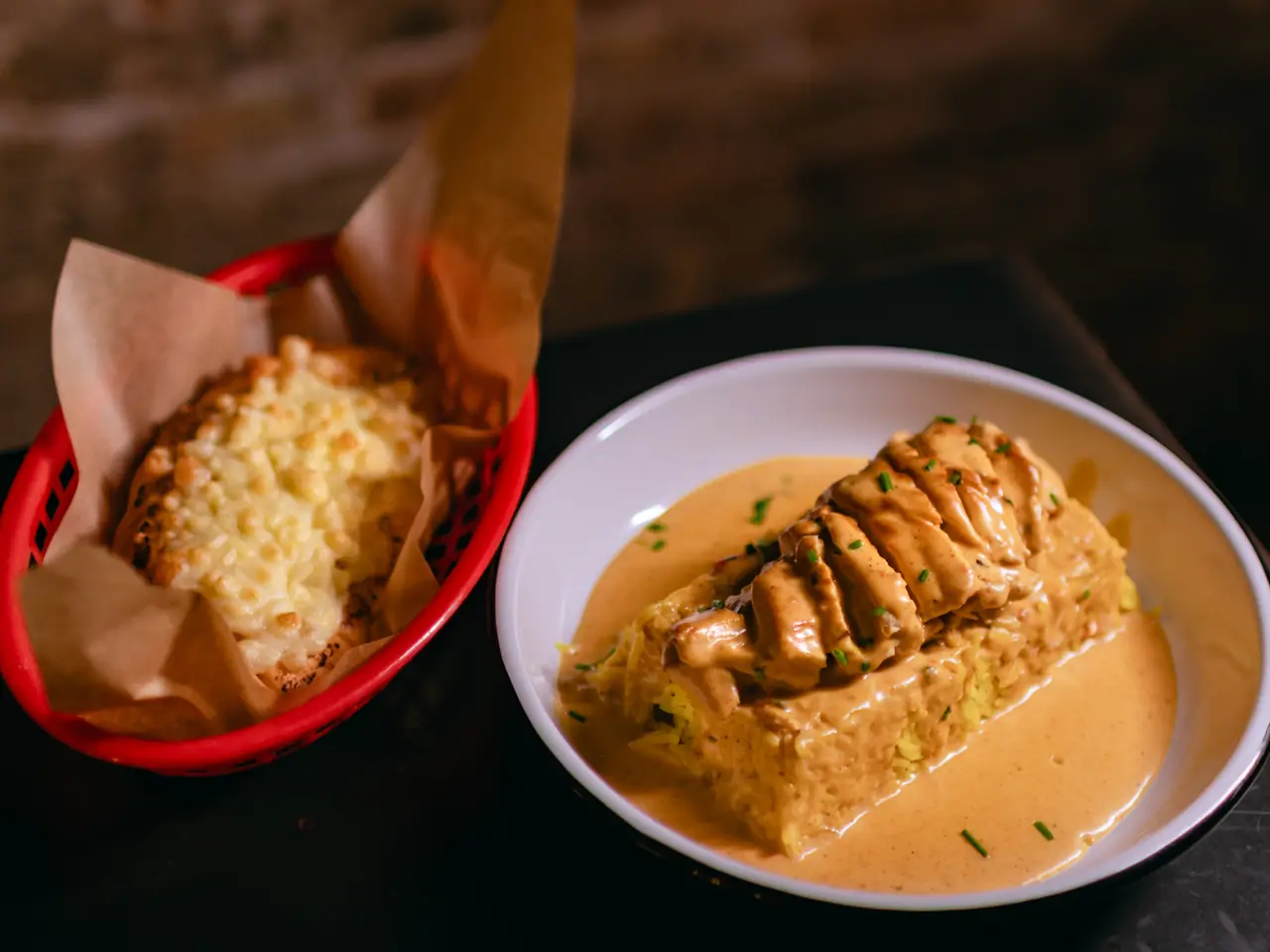 A creamy curry-sauced dish with sliced meat over rice on a white plate, served alongside a cheese-topped bread in a red basket, at Spice BCN