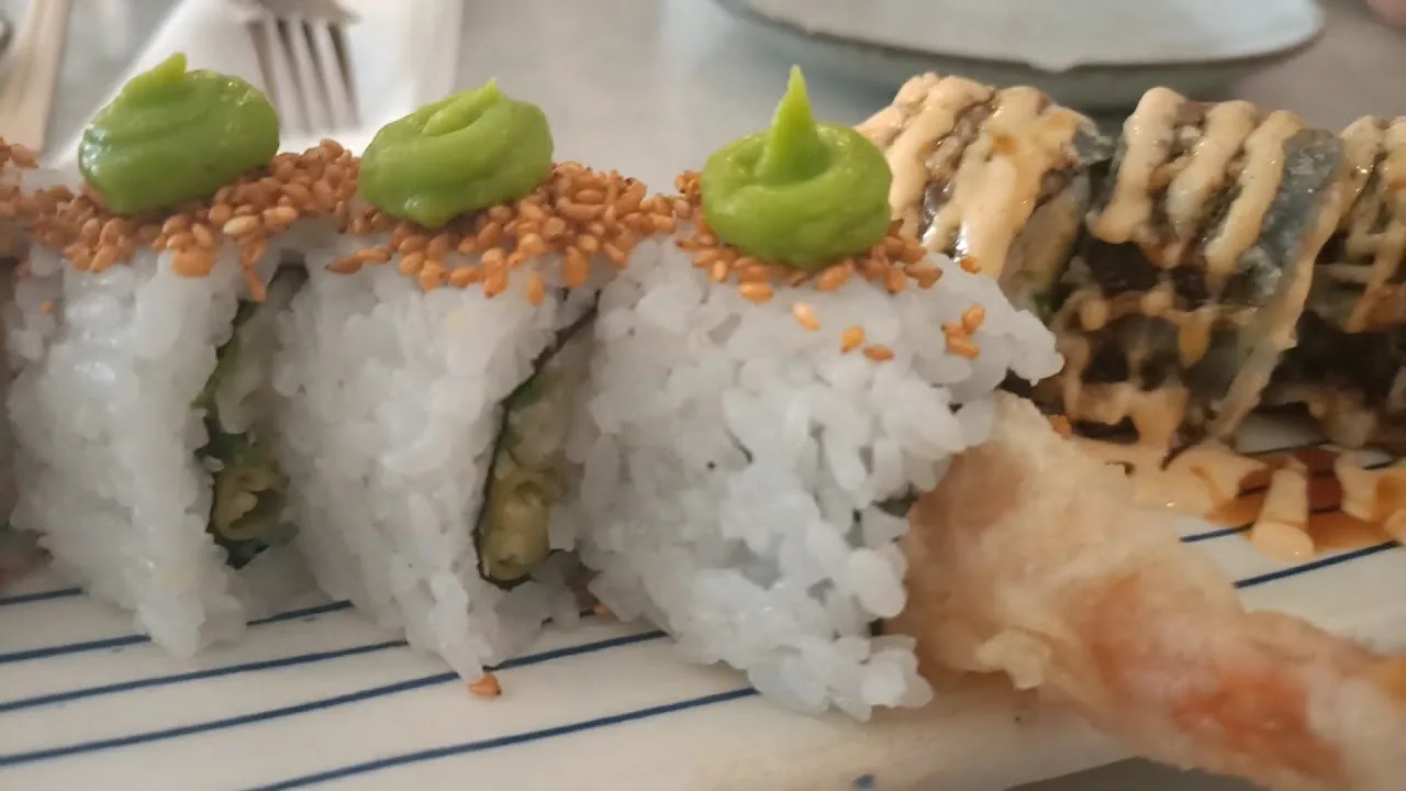 Rice rolls topped with wasabi and a tempura prawn on a white plate