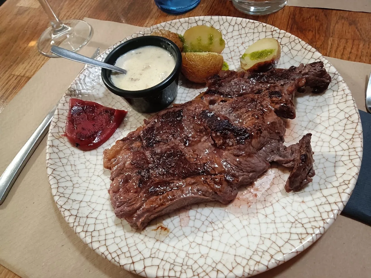 A grilled steak with a side of white sauce on a patterned plate