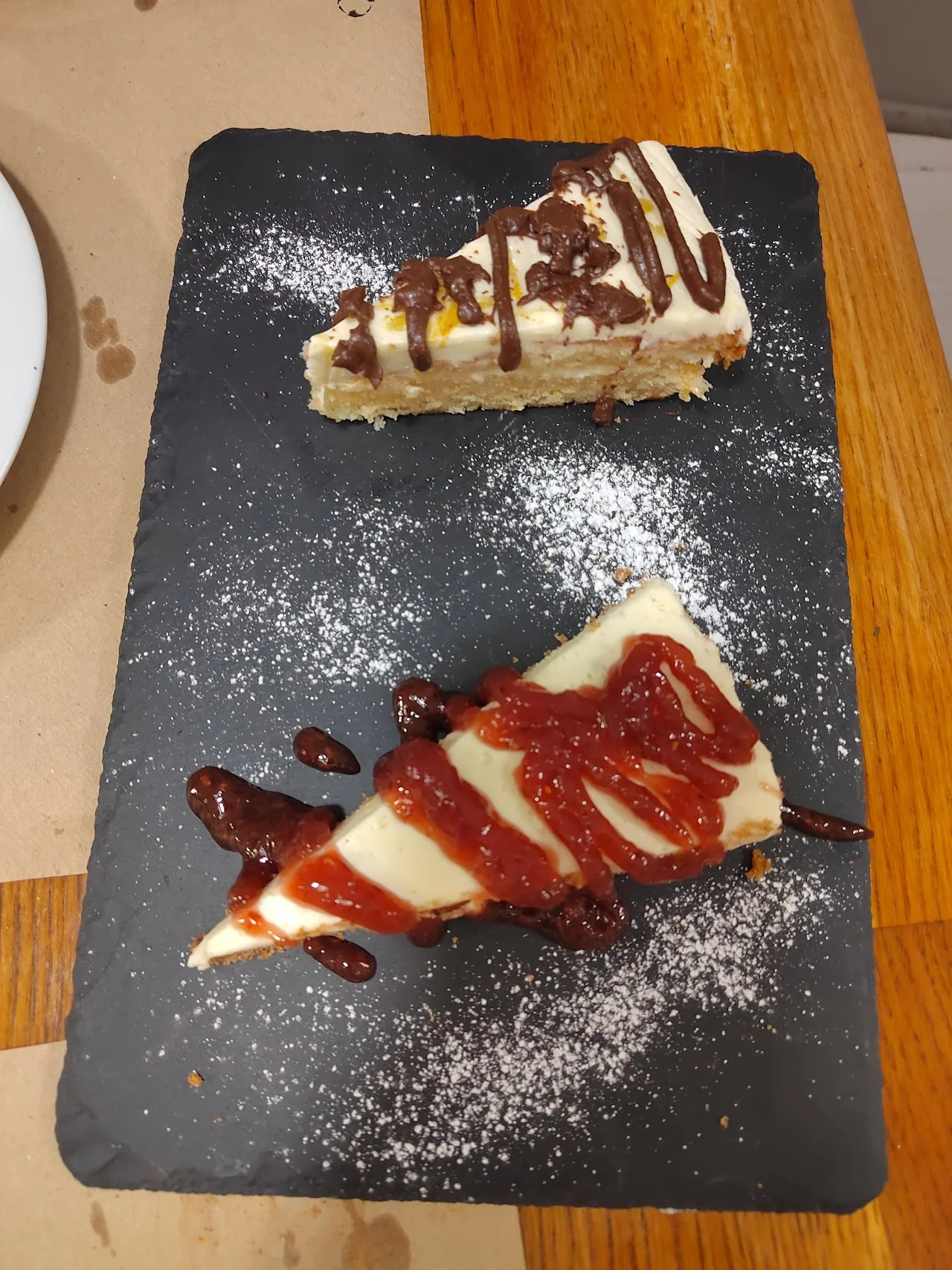 Two slices of cheesecake with a berry drizzle on a dark slate board