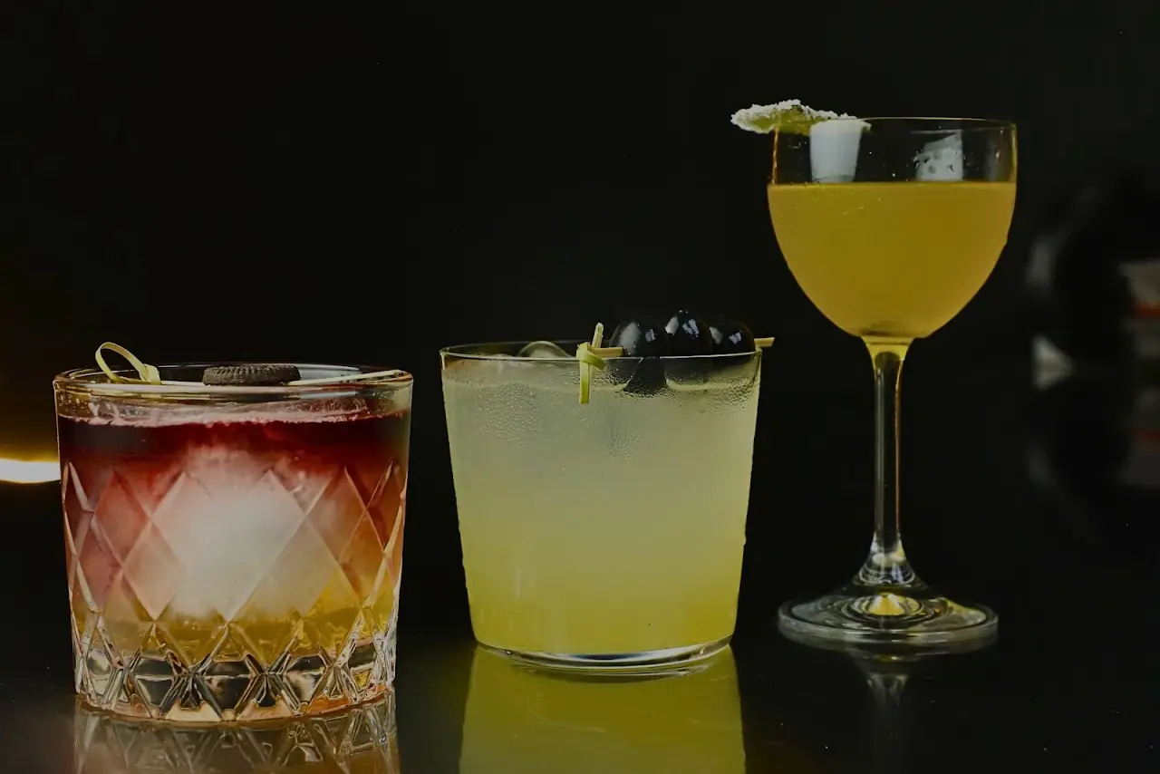 Three different cocktails lined up on a dark bar counter.