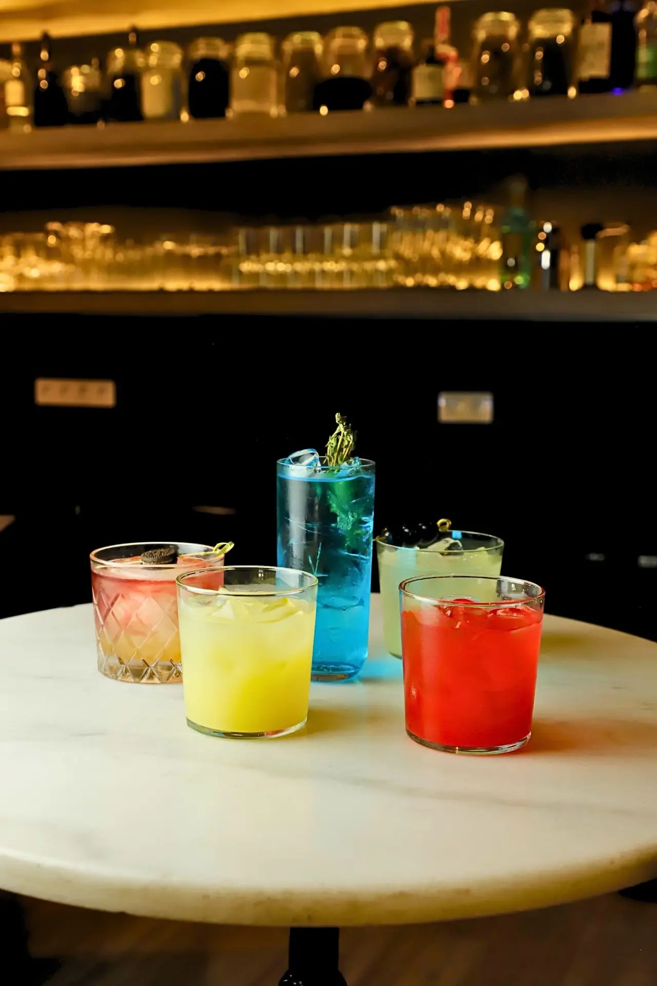 Three colorful cocktails, blue, yellow and red, set on a small marble table.