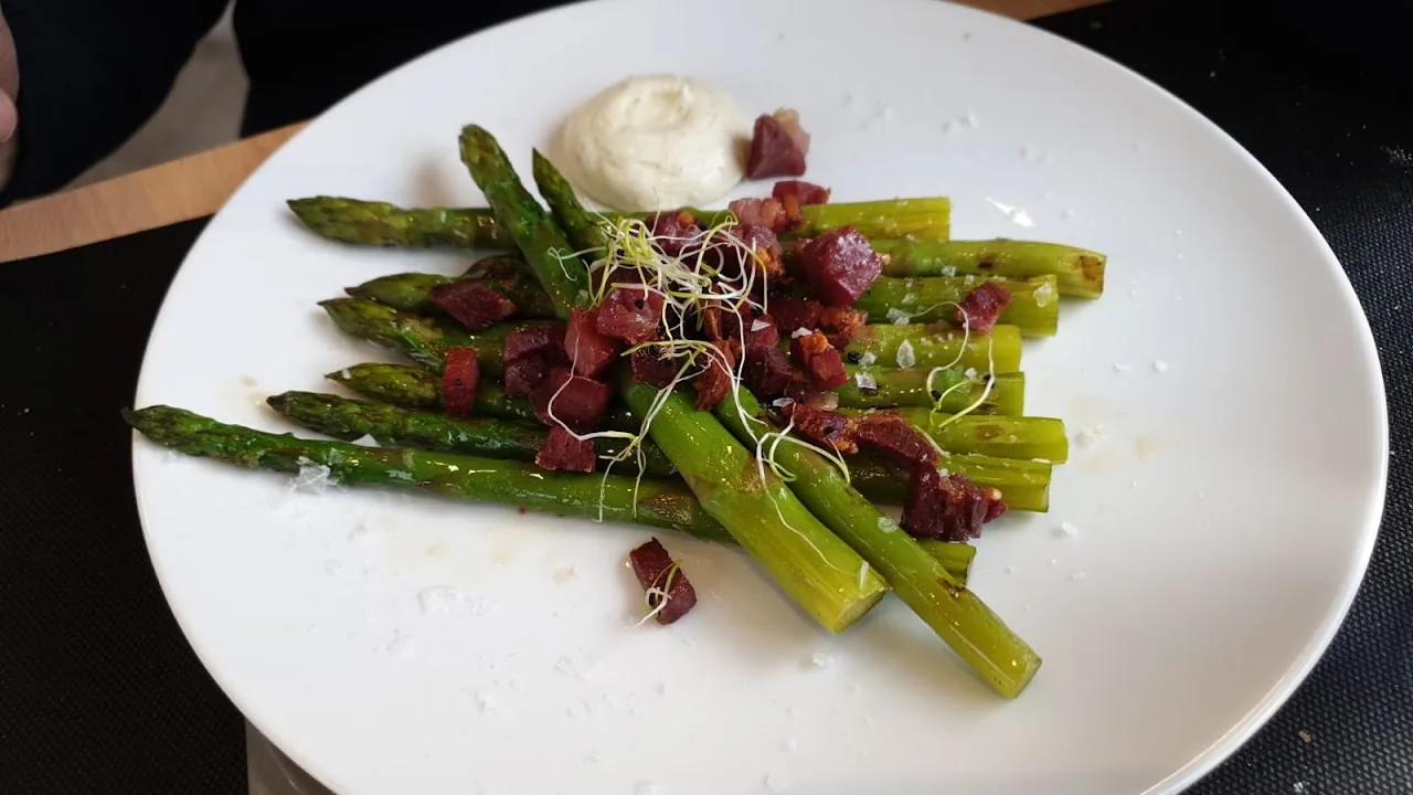 A plate of grilled green asparagus with cured ham and a cream sauce