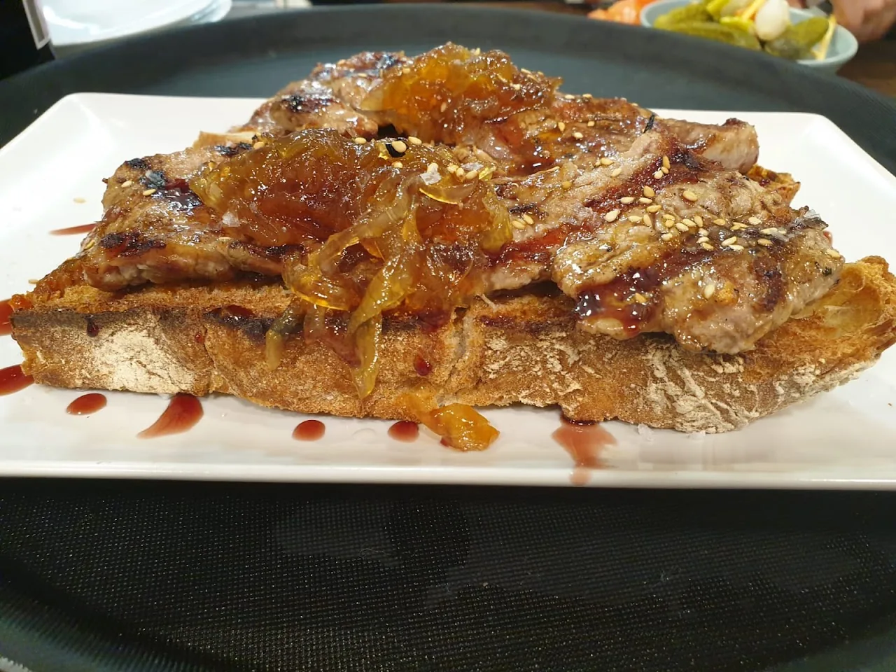 A grilled flatbread topped with shredded meat and sesame seeds