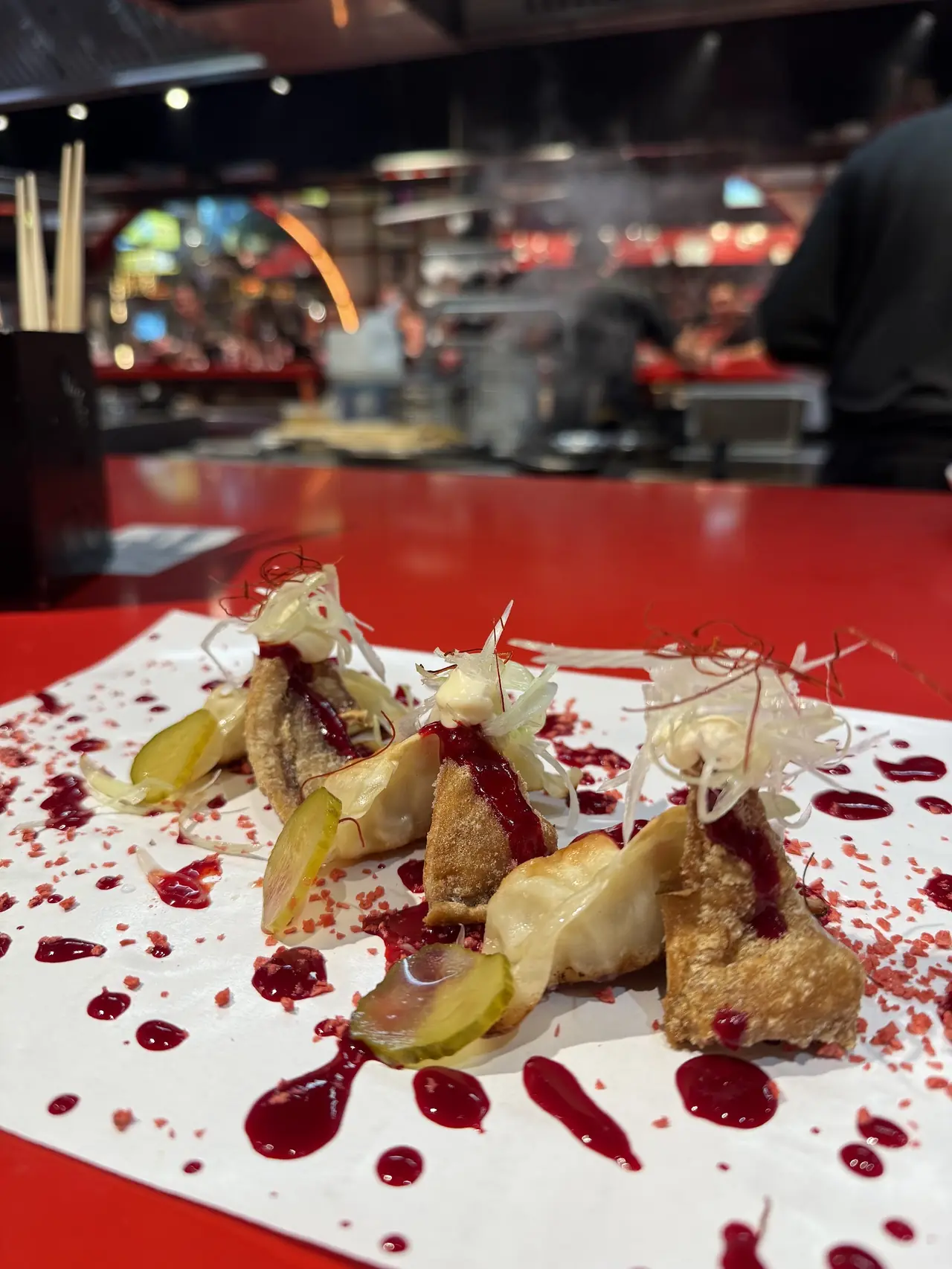 Fried dumplings with pickles, berry sauce and shaved fennel garnish on paper at bar counter