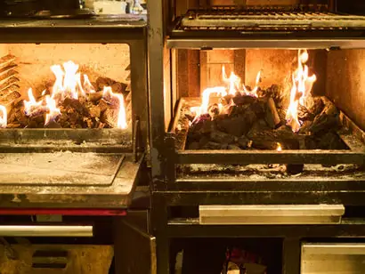 Two open charcoal-fired grill ovens burning with live flames and embers in the venue's kitchen