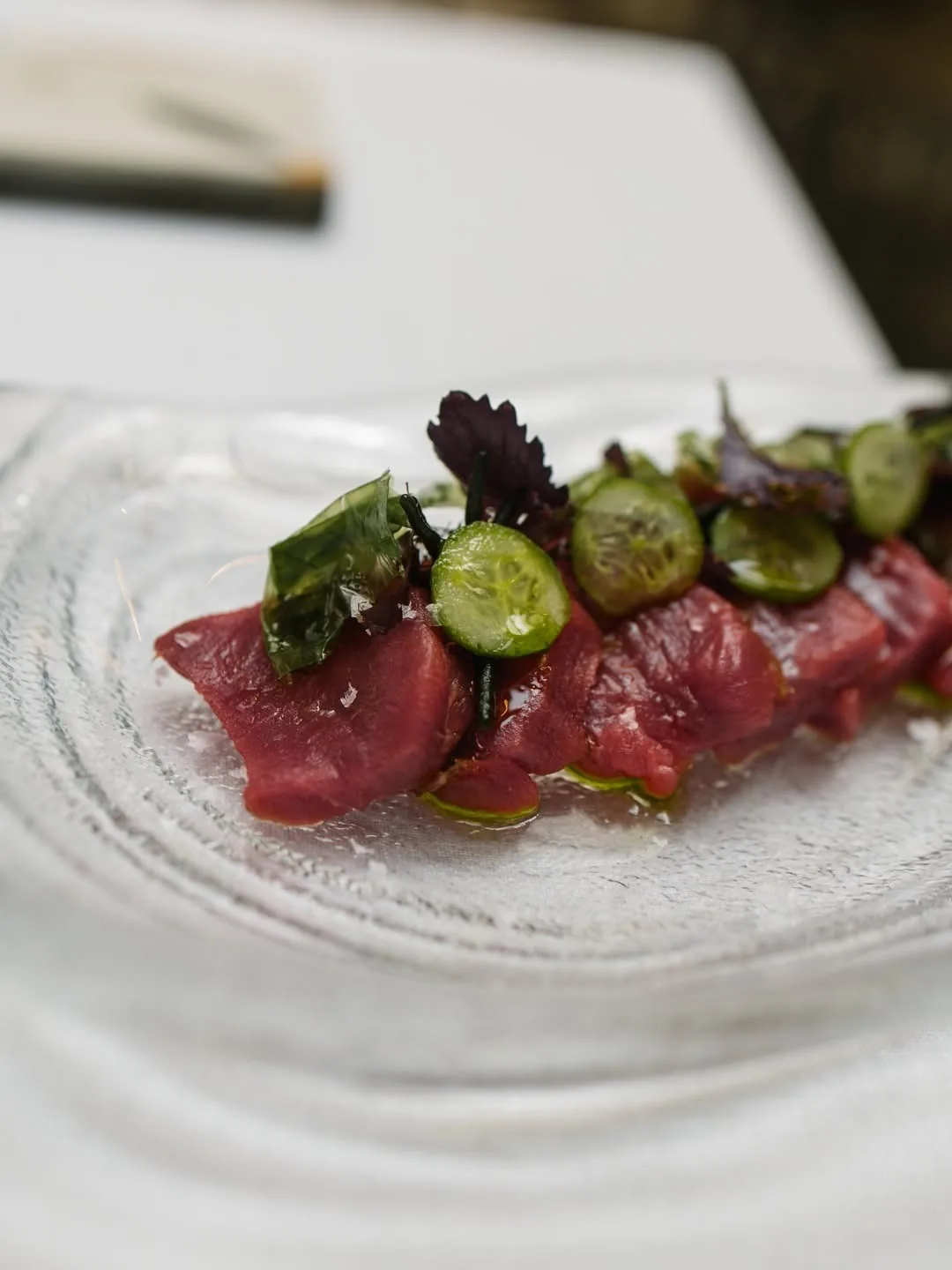 Slices of raw red tuna with small green pieces on a white plate