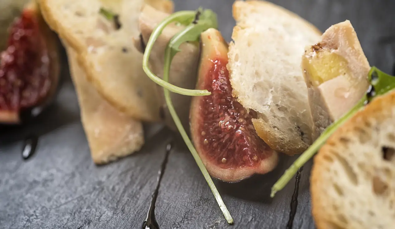 Sliced fresh fig and toasted bread with a drizzle of balsamic reduction on a slate board, at Sucapa