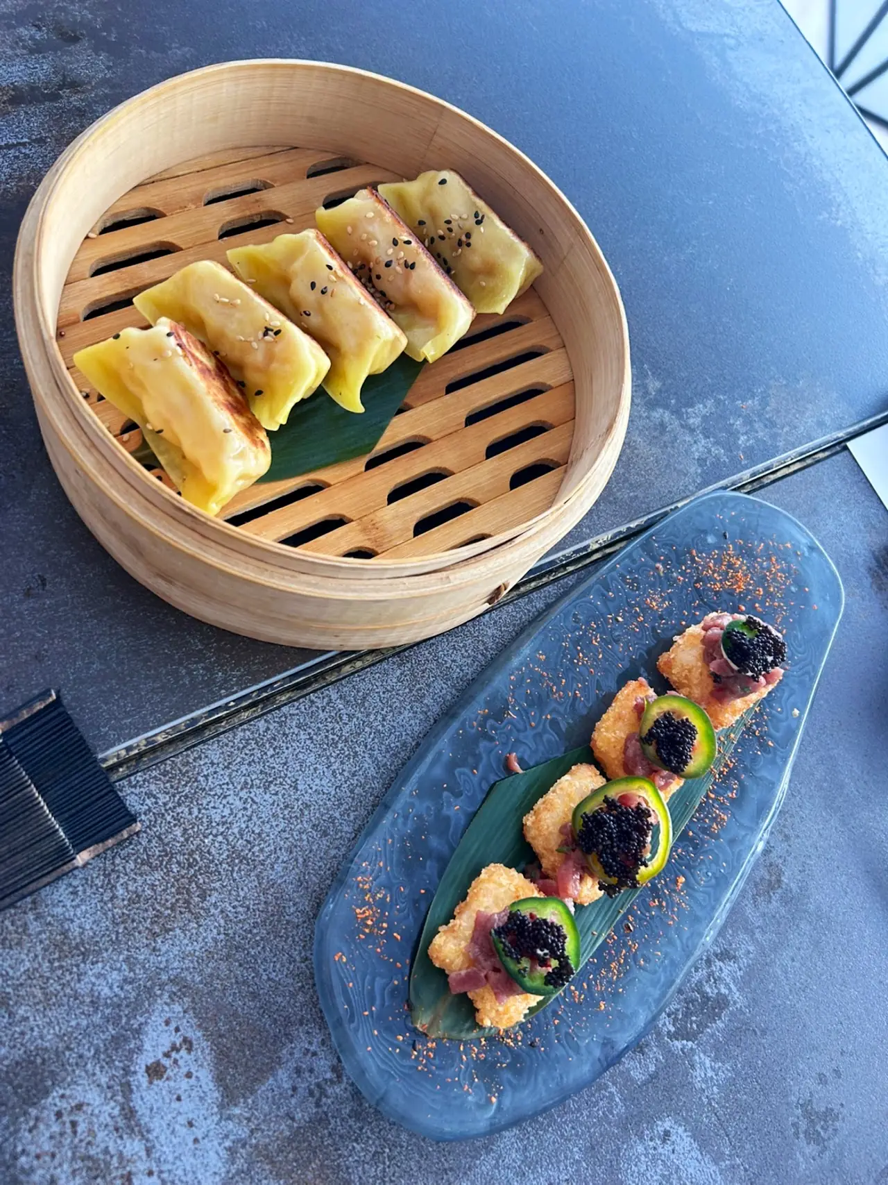 Steamed dumplings in a bamboo steamer beside a plate of garnished rolls