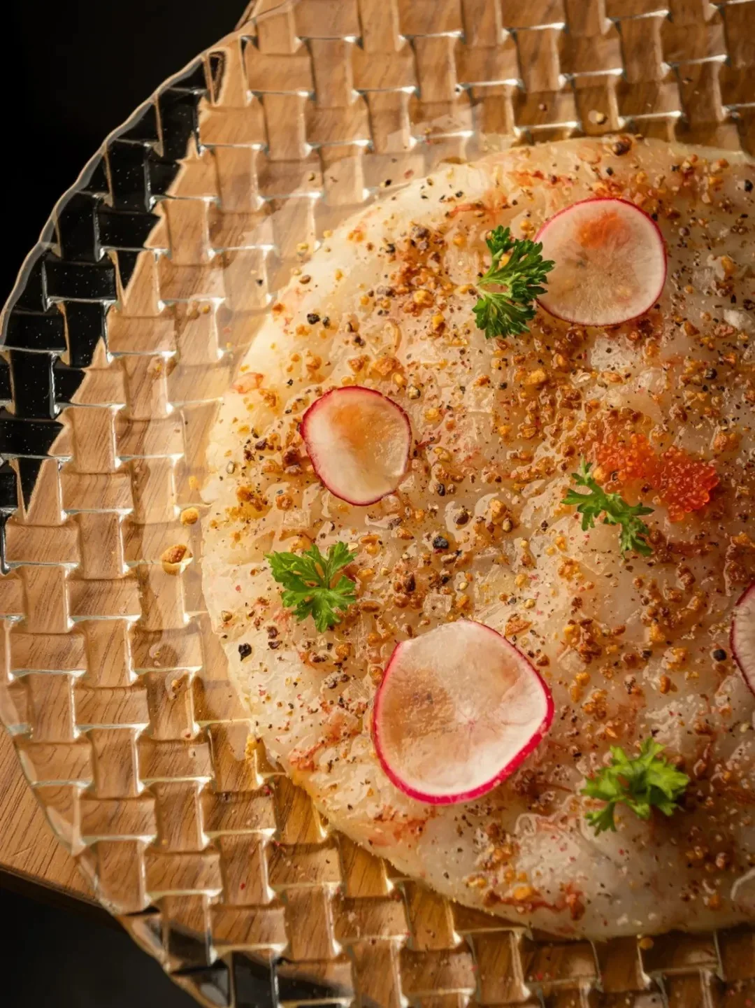 A pale round crisp topped with radish slices and herbs on a woven mat