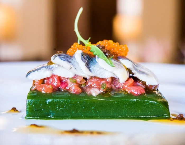 A small piece of marinated fish topped with orange roe on a green base