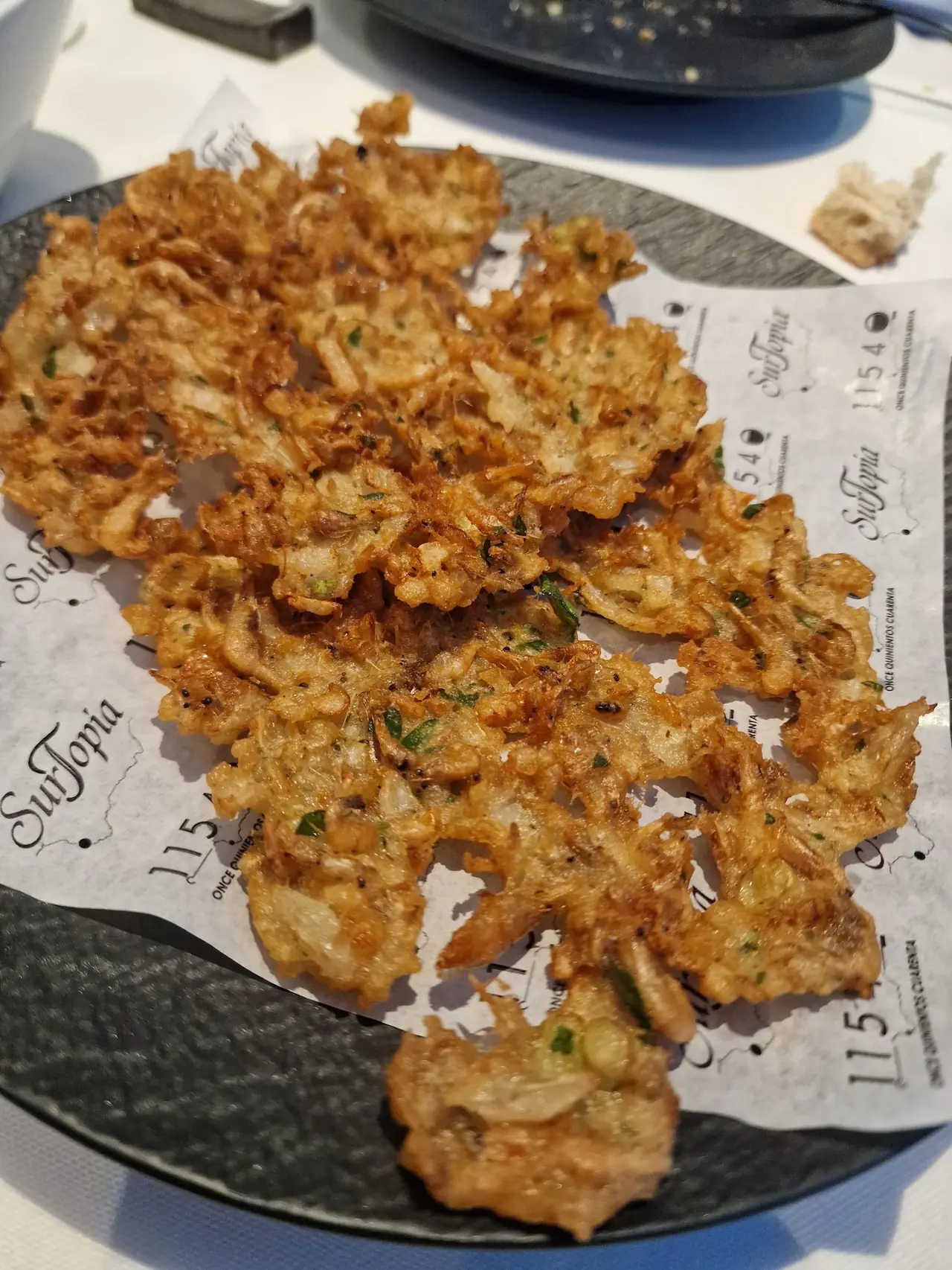 Pile of thin fried shrimp fritters on branded paper on a dark plate