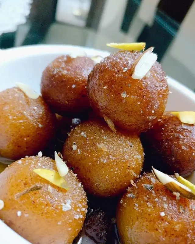 Close-up of gulab jamun, fried dough balls in syrup topped with slivered nuts, in a white bowl at Swad - The Indian Restaurant