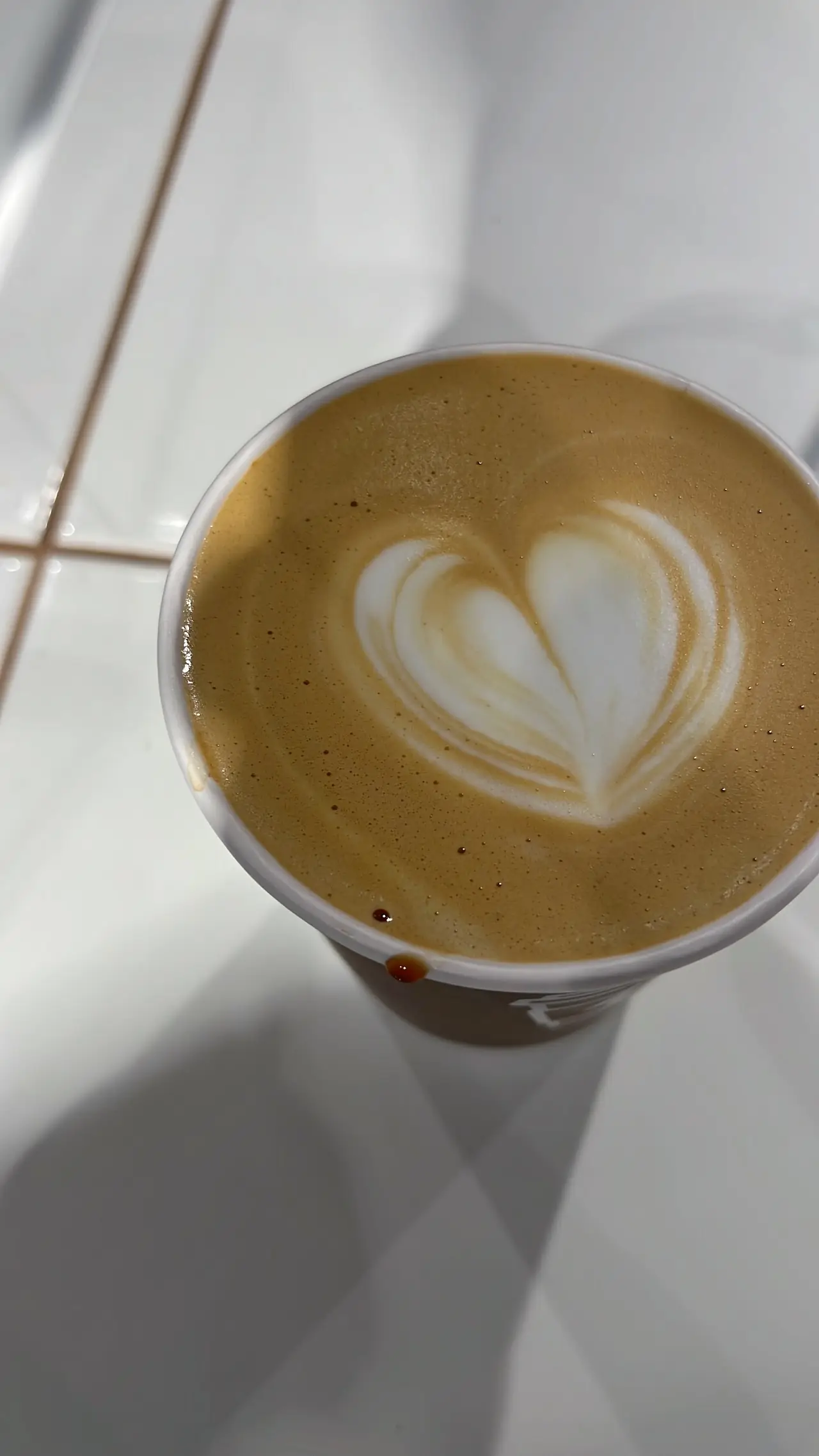 Overhead view of a latte with heart-shaped latte art in a white cup.