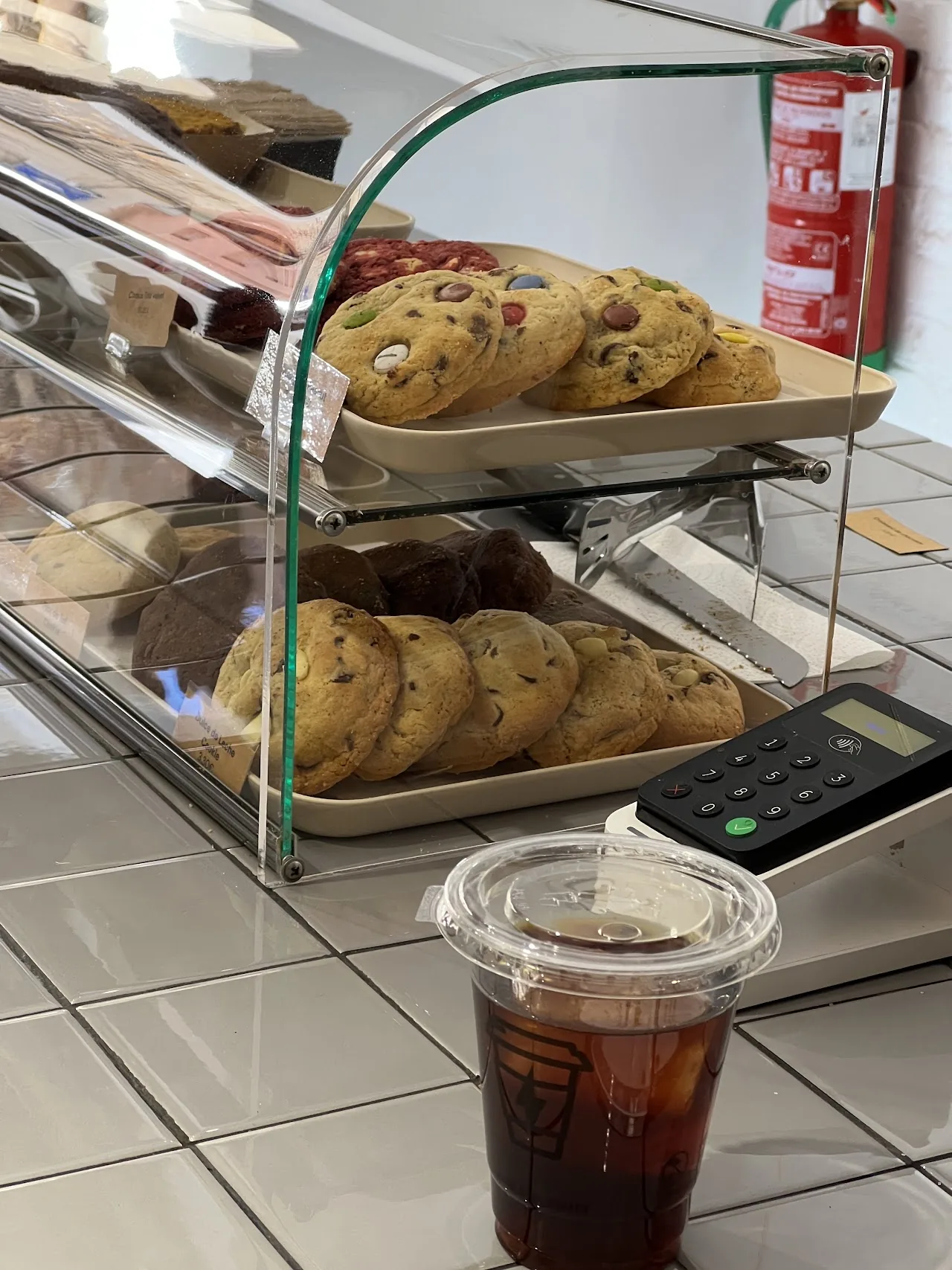 An iced coffee cup on a counter beside a bakery display of pastries