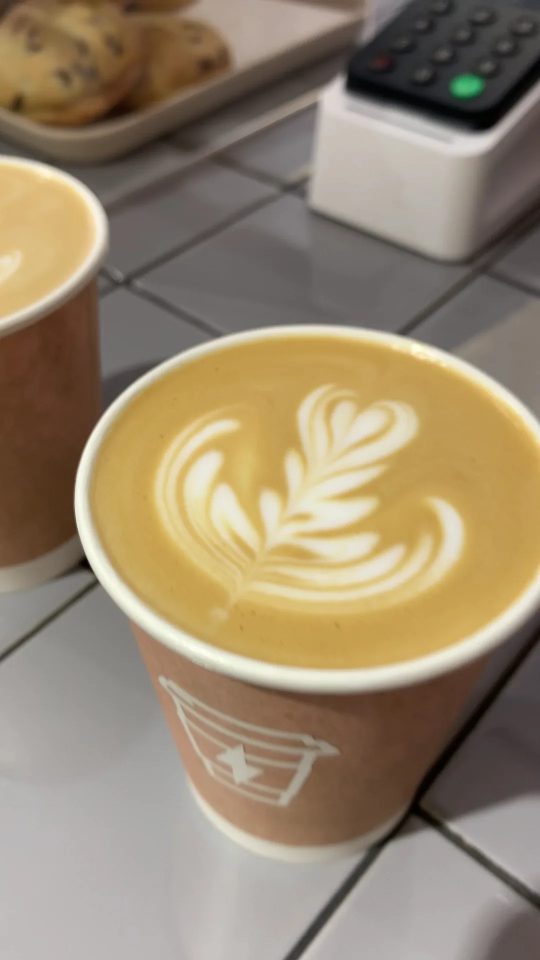 A latte with a leaf-pattern foam design in a paper cup