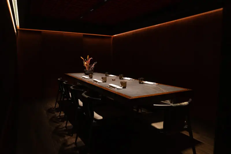 Dimly lit private dining room with a long dark table set for eight, black chairs and warm accent lighting