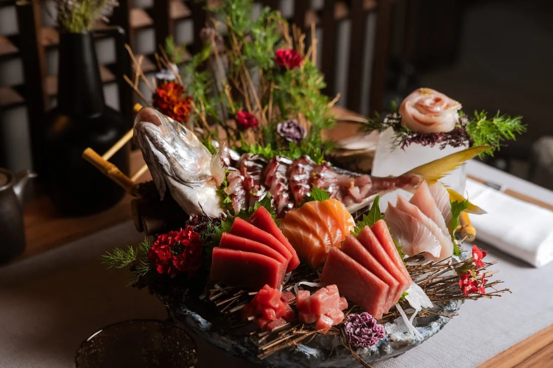 A platter of sashimi, red tuna slices and garnishes on a wooden tray