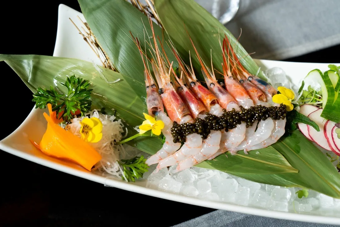 Raw shrimp sashimi laid on green leaves on a white plate