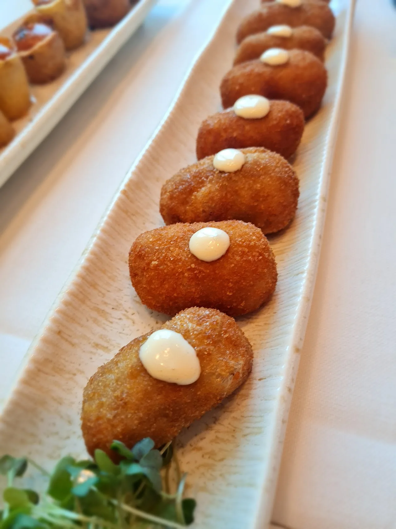 A row of croquettes with a dollop of sauce on each, on a long plate