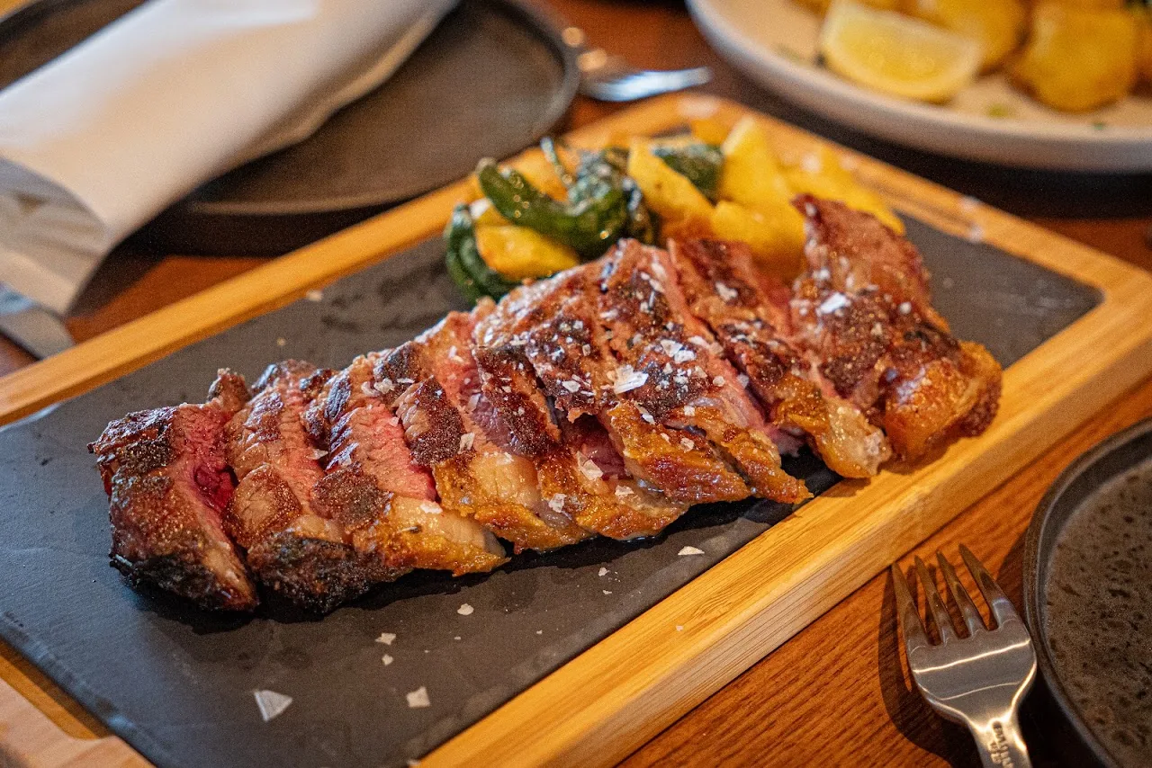 Sliced grilled meat on a wooden board with charred peppers