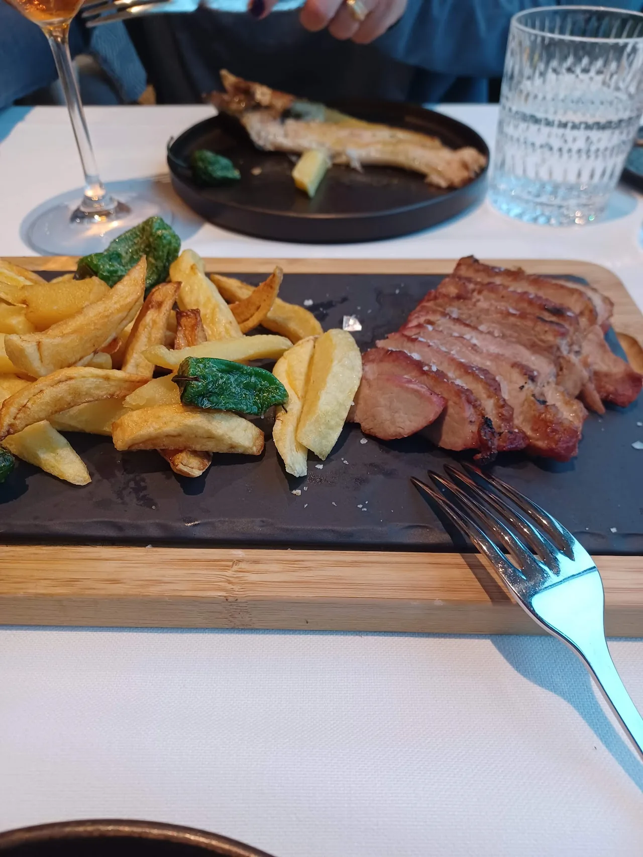 A grilled steak with fries and sauteed greens on a slate board