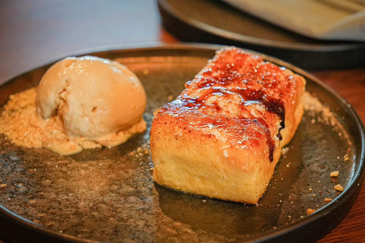 A thick caramelised slice of bread with a scoop of ice cream beside it on a dark plate