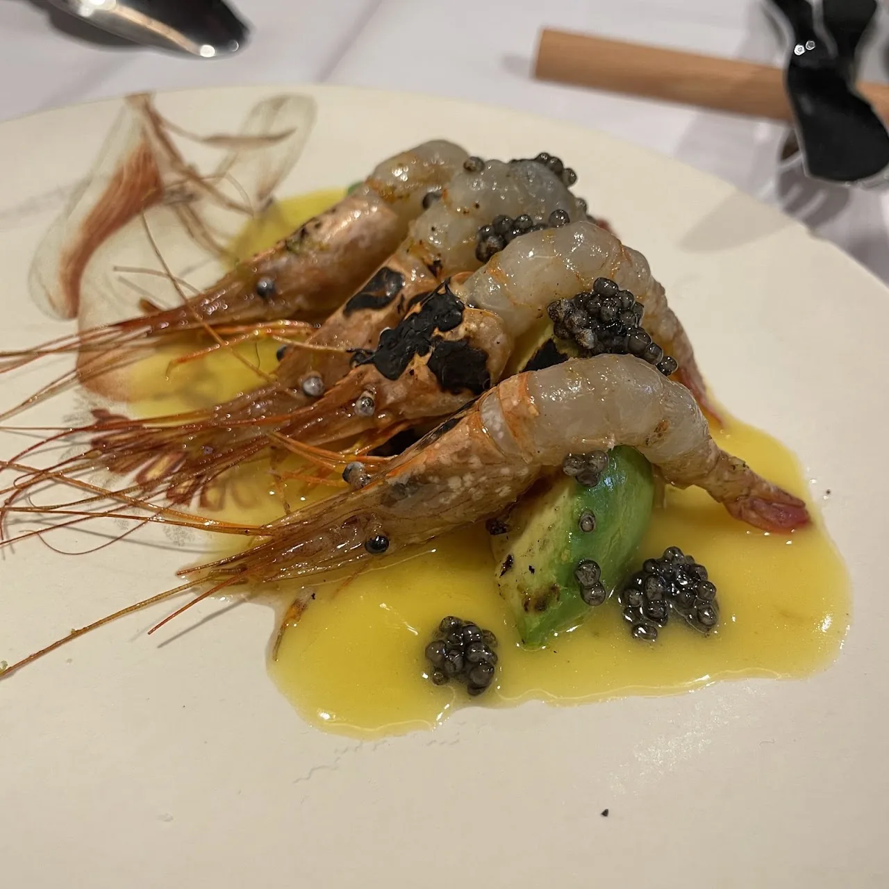 A plate of grilled prawns with black caviar in a citrus butter sauce