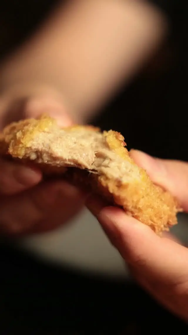 Hands tearing open a piece of breaded fried food, showing the interior