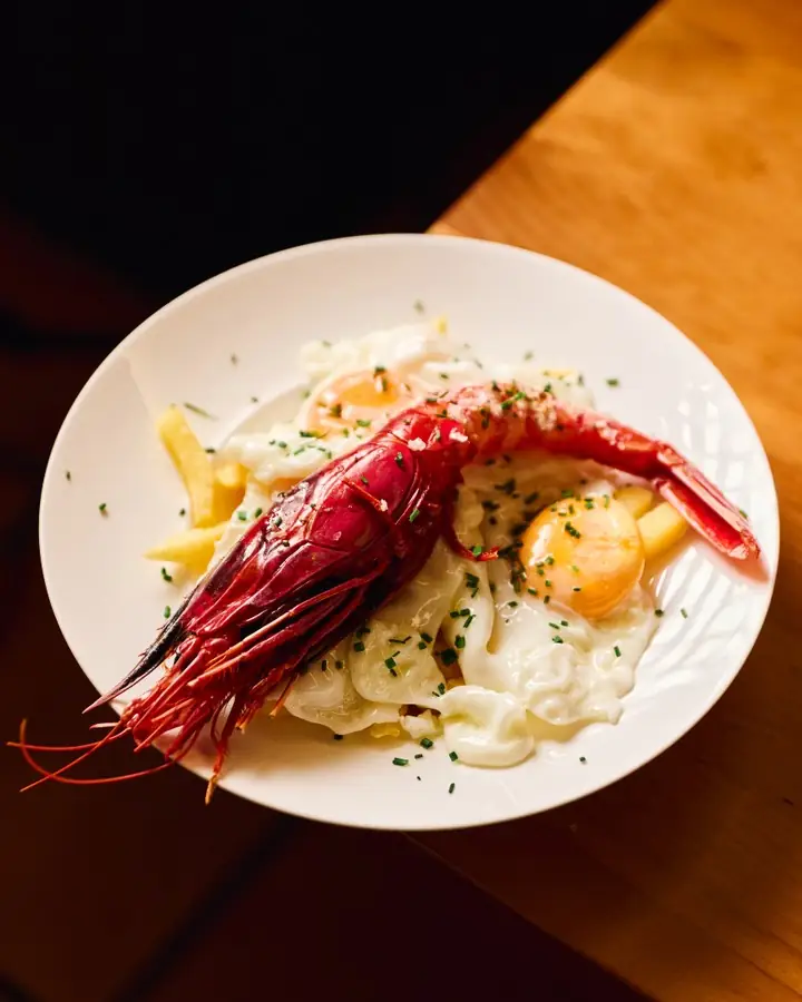 Fried eggs with a large red shrimp and fries on a plate