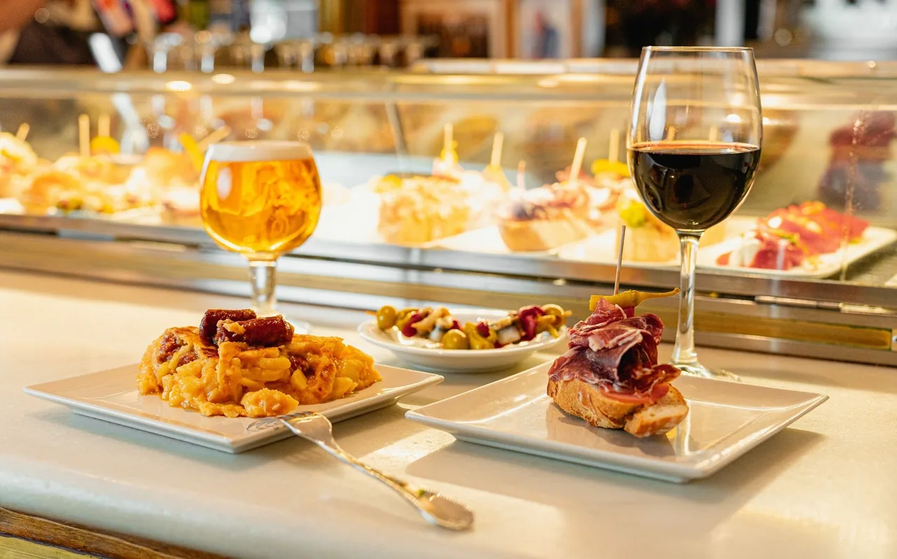 A bar counter with small tapas plates and glasses of beer and red wine