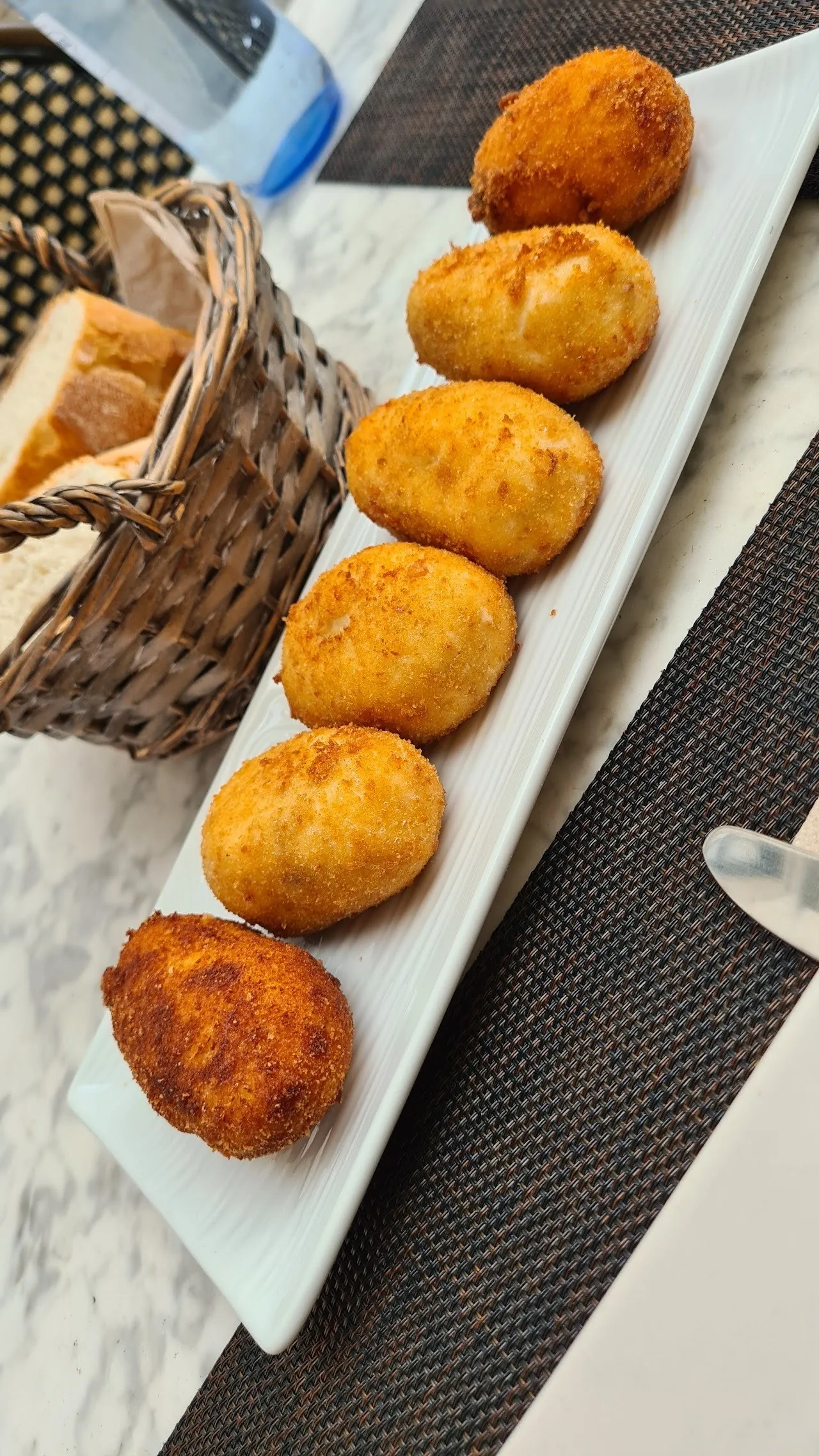 Golden croquettes on a long white plate beside a bread basket