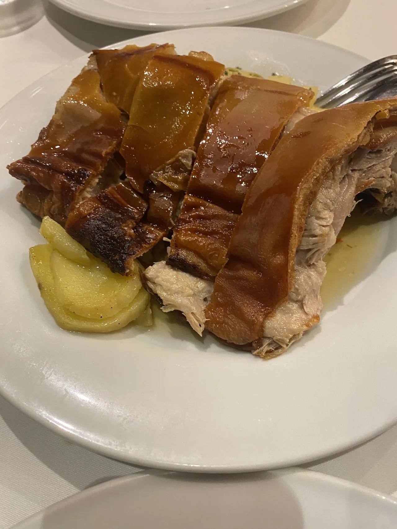 Sliced roast suckling pig with glossy crackling skin and sliced potatoes on a white plate