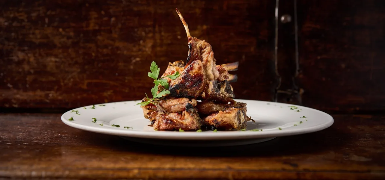 A plate of lamb chops with a garnish on a dark wooden surface