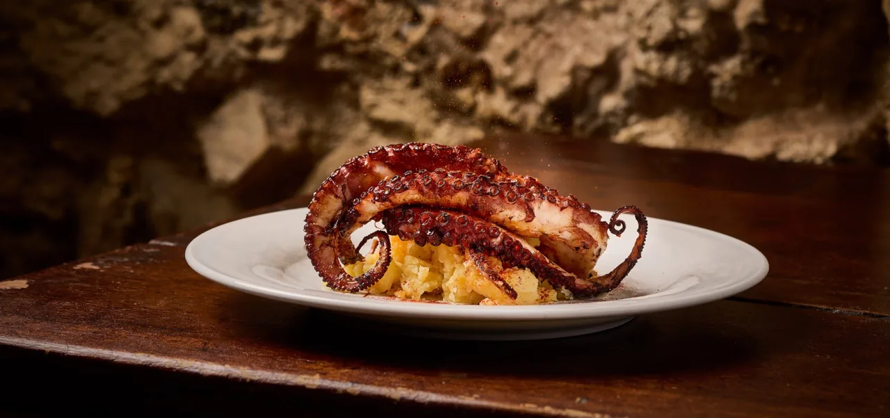 A plate of octopus tentacle over potato on a dark wooden surface